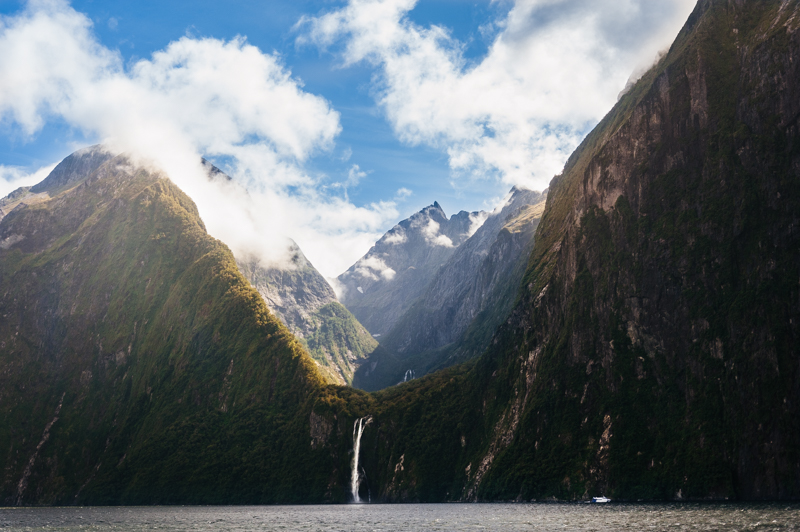 Serene view of Milford Sound with misty mountains, a waterfall, and boat in New Zealand